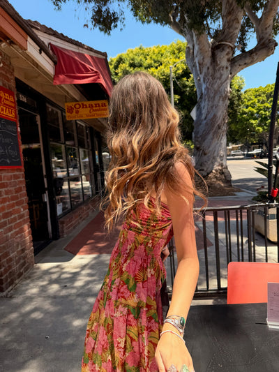 Woman in a pink dress standing on a sidewalk with a tree and storefronts in the background