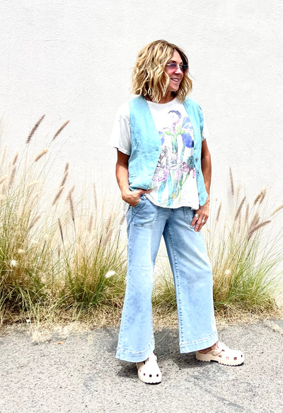 Person wearing a colorful shirt and light blue jeans standing in front of tall grass.