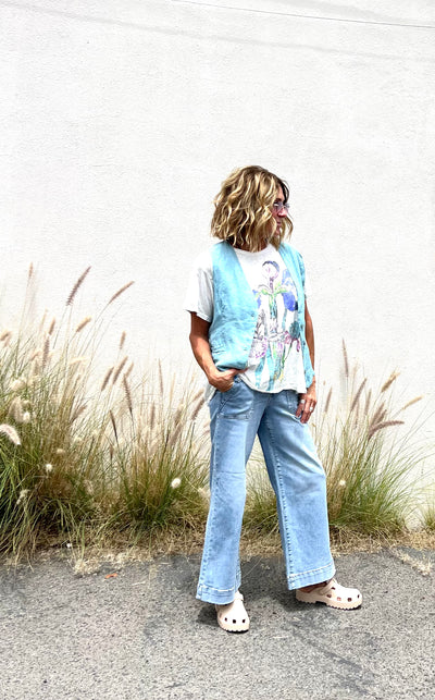 Person wearing a light blue vest over a colorful shirt with floral patterns, standing outdoors with tall grasses in the background.