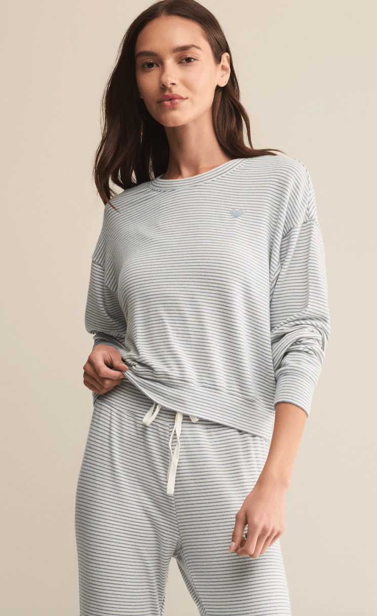 Woman wearing a light gray striped long-sleeve top and pants on a beige background