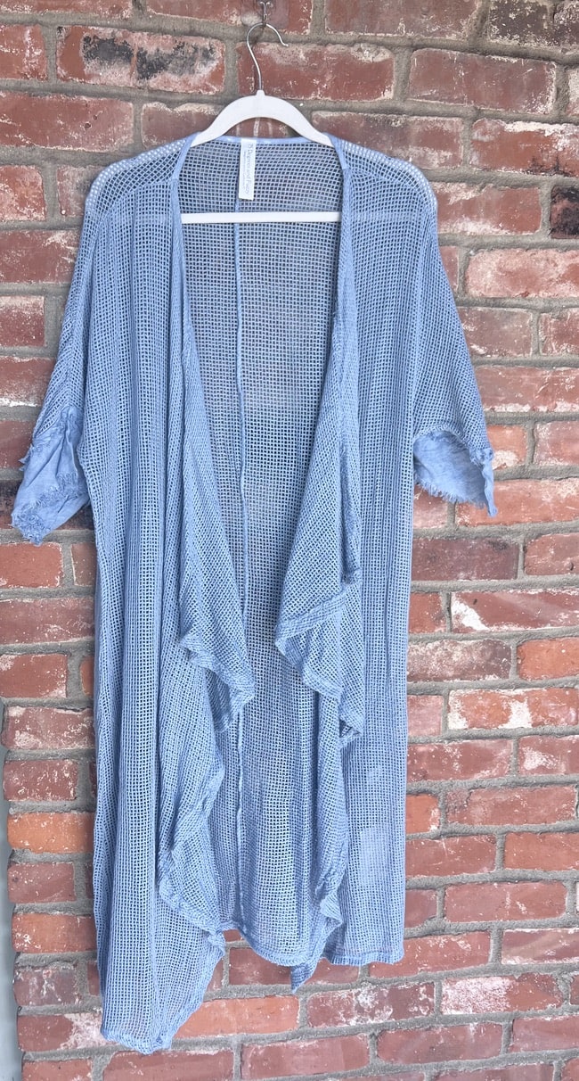 Blue mesh dress on a hanger against a brick wall