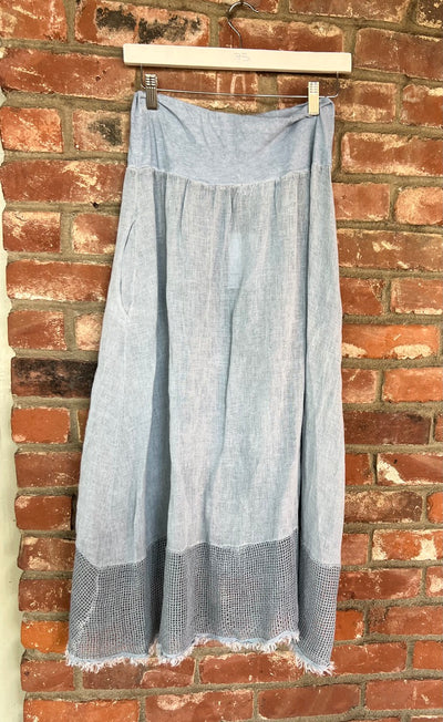 Light blue denim pants hanging on a wooden hanger against a brick wall.
