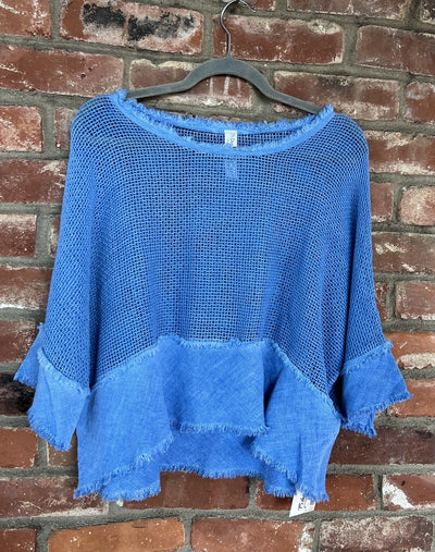 Blue knit top on a hanger against a brick wall