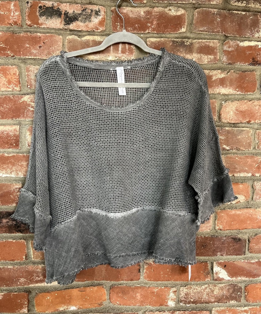 Gray knit sweater on a hanger against a brick wall