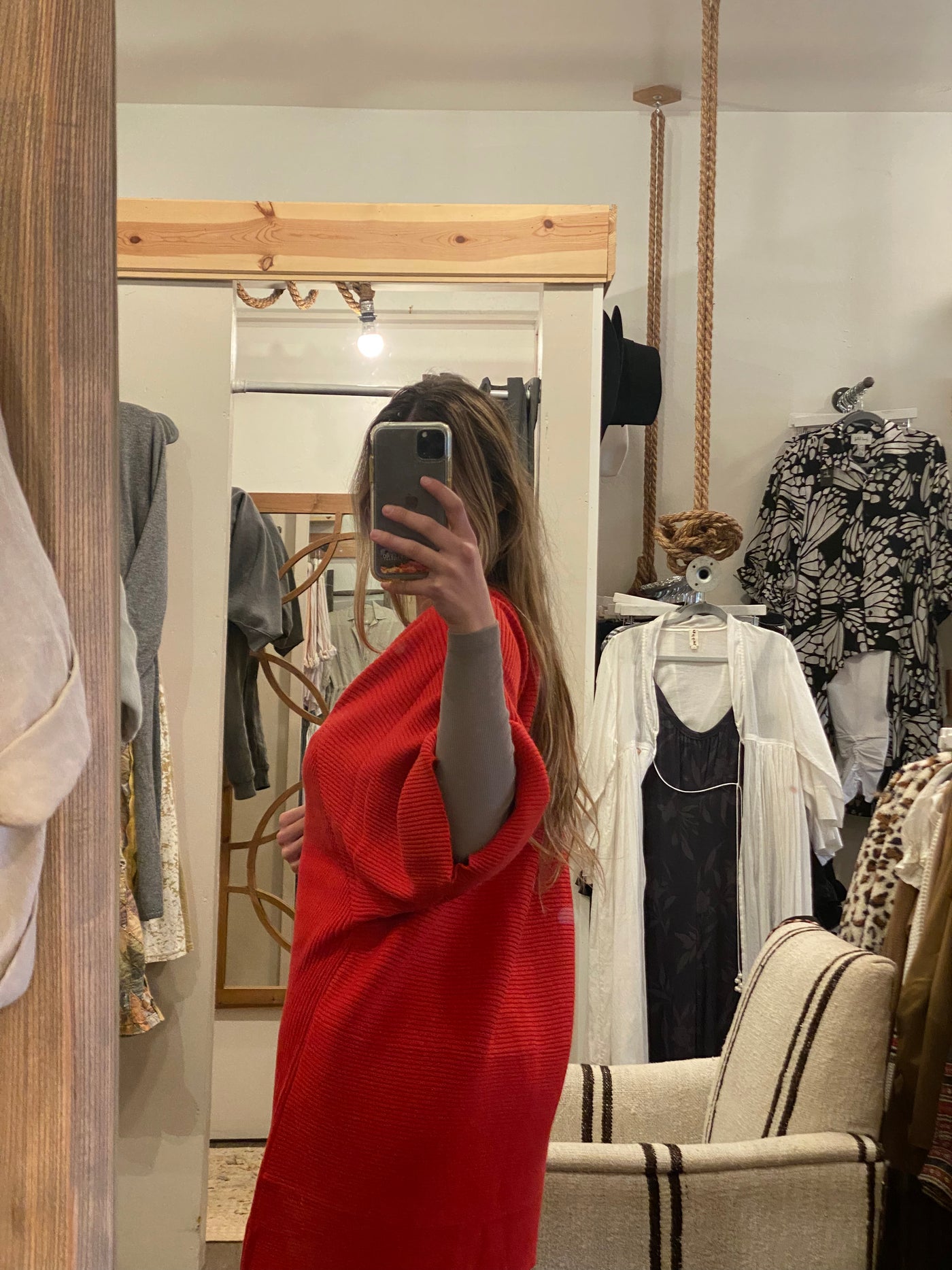 Girl standing backwards with long blonde hair taking a picture of herself in a mirror with a scarlet cardigan sweater