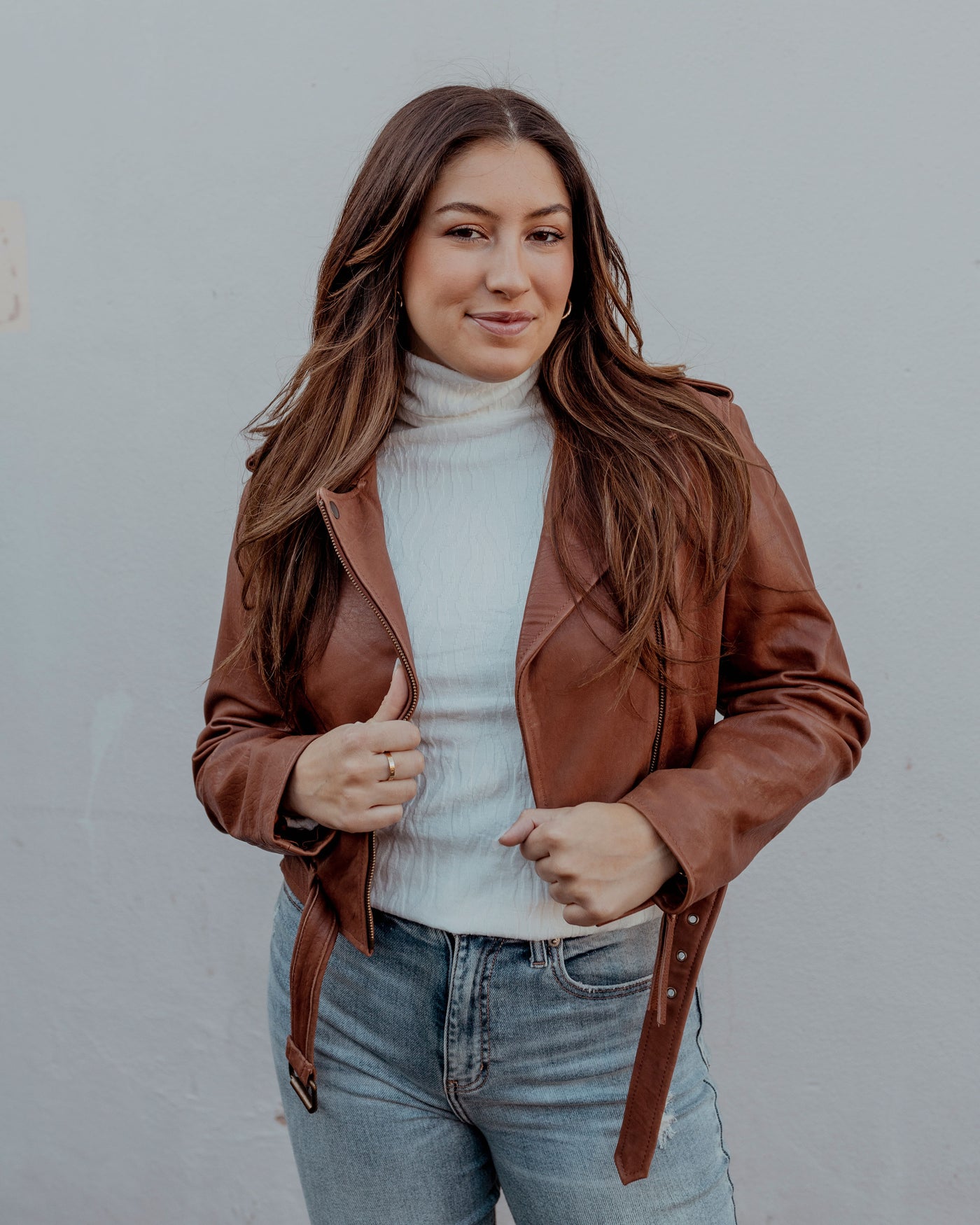 Girl with long brown hair in a motto leather coat that is brown with a white wavy textured  turtleneck