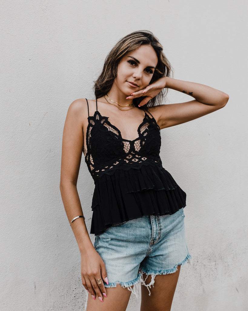Brown haired girl with her hand under her face standing in a black eyelet strappy top