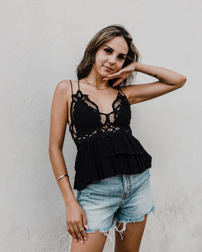 Brown haired girl with her hand under her face standing in a black eyelet strappy top